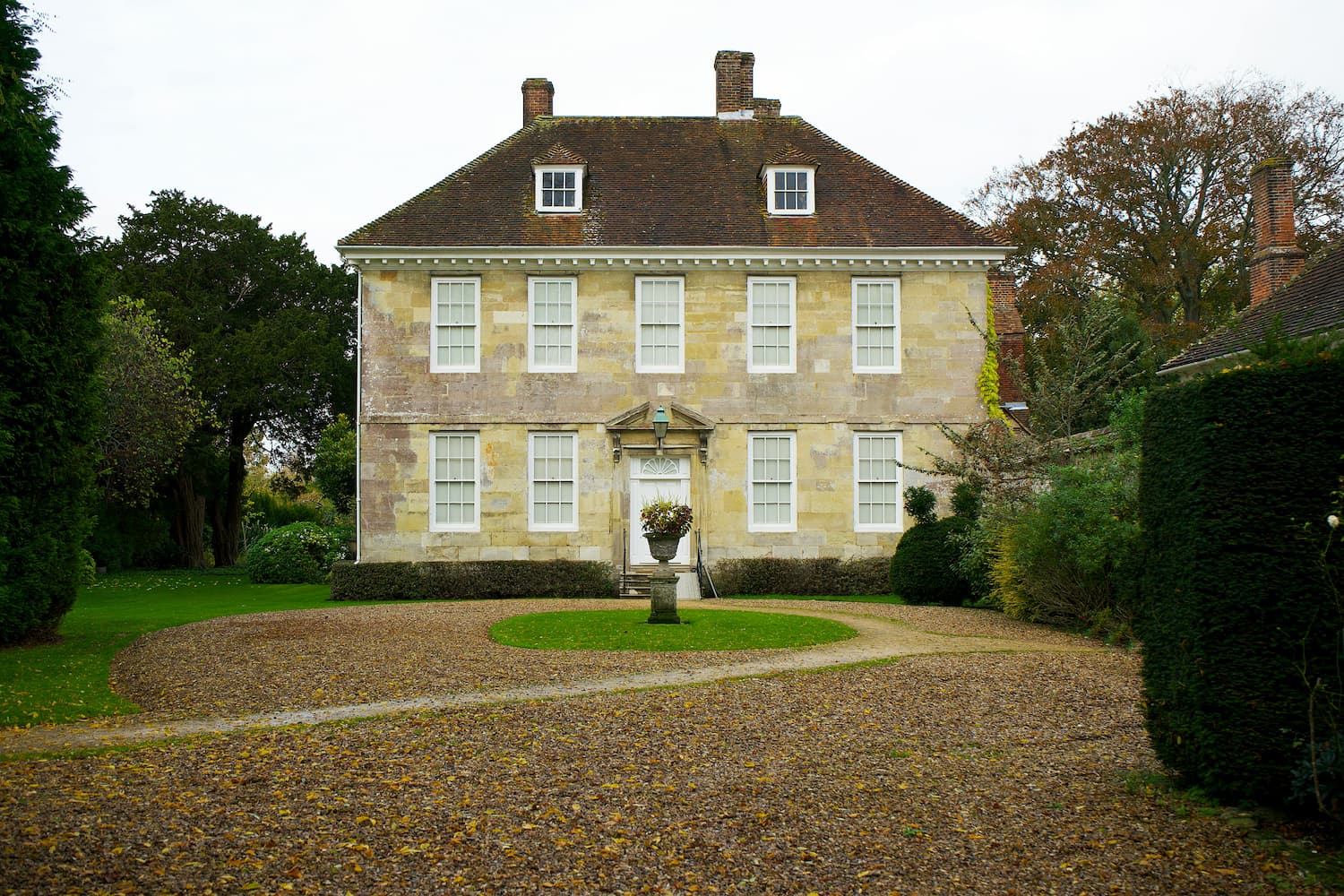 a large sandstone house in the UK with a gravel driveway and plenty of surrounding greenery